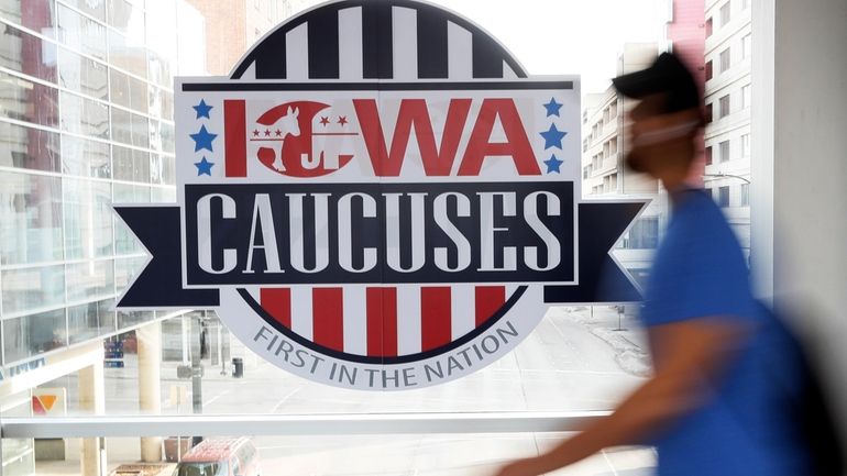 A pedestrian walks past a sign for the Iowa Caucuses...