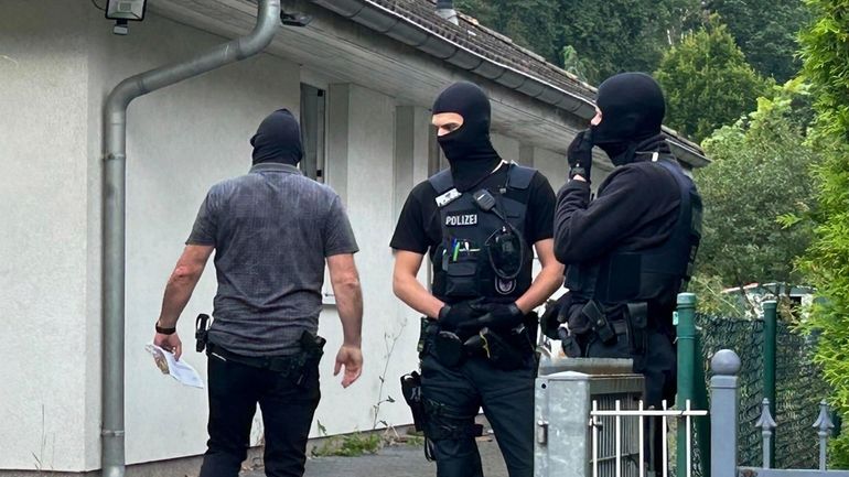 Masked police officers stand in front of a house in...