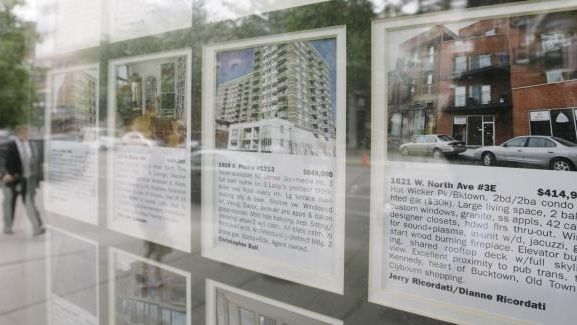 A pedestrian walks past windows filled with real estate listings...