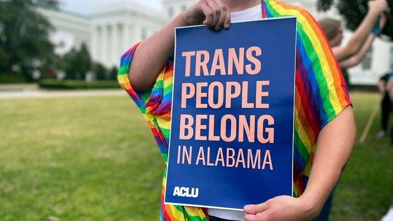 A person holds up a sign reading, "Trans People Belong...