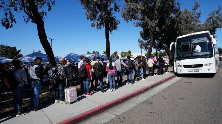 Migrants line up to take a bus to the airport...