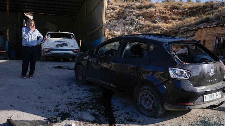 Palestinians look at a damaged car following an Israeli airstrike...