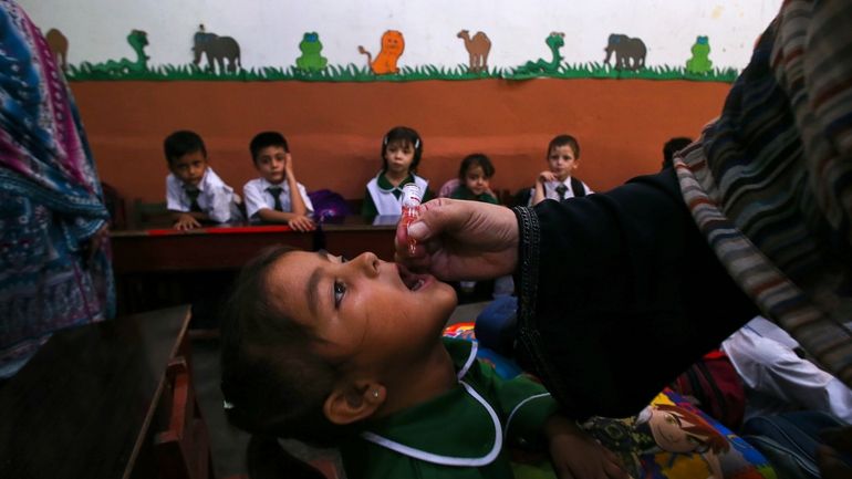 A health worker administers a polio vaccine to a child...