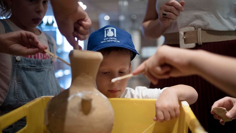 Ariel Heller, 4, helps to glue a broken clay jar...