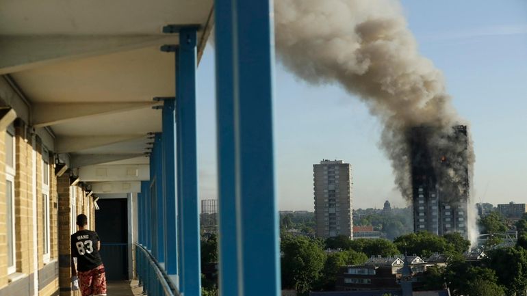 A resident in a nearby building watches smoke rise from...