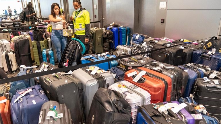 An airline employee, right, helps a traveler find her suitcase...