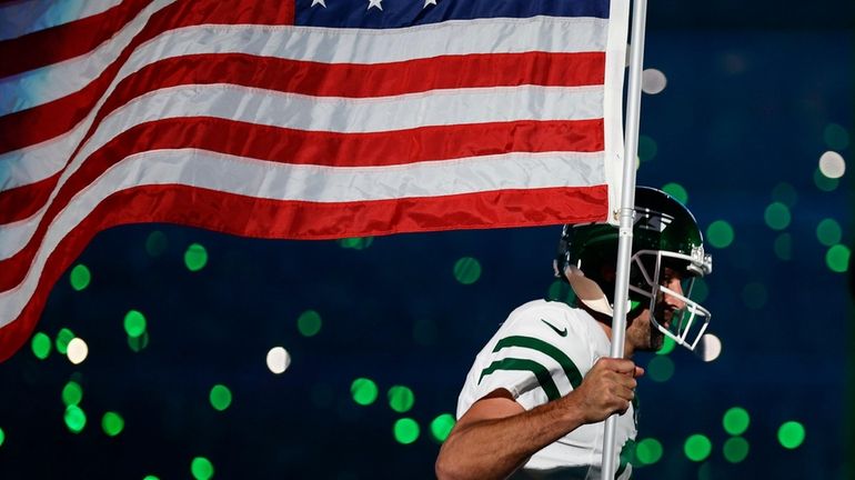 Jets quarterback Aaron Rodgers carries an American flag onto the...