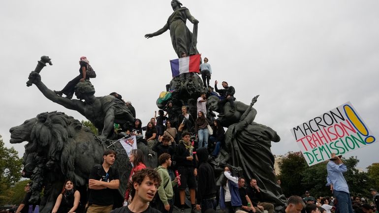 Demonstrators, one displaying French flag, gather under the statue of...