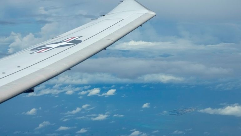 A U.S. P-8A Poseidon reconnaissance plane flies near Chinese structures...