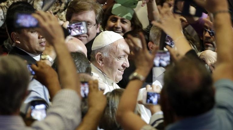 Pope Francis is surrounded by people taking pictures