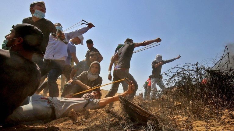 Palestinian protesters use slingshots to hurl stones toward