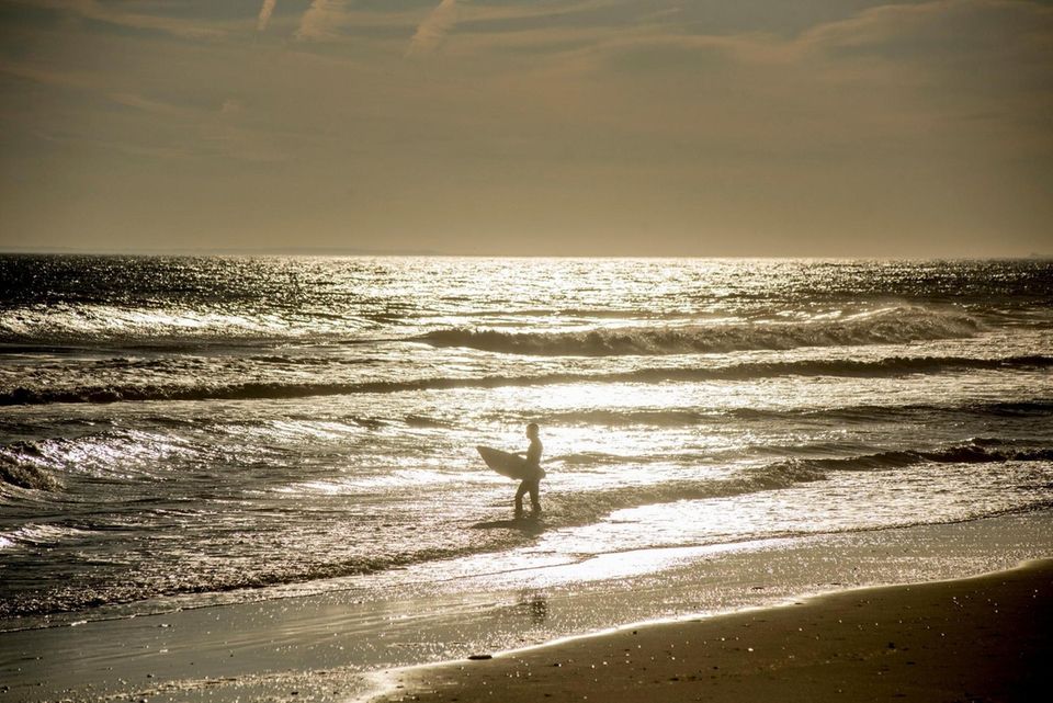 A surfer wades into the Atlantic Ocean off