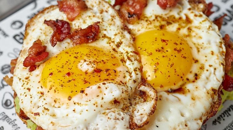 Avocado toast topped with eggs and bacon at