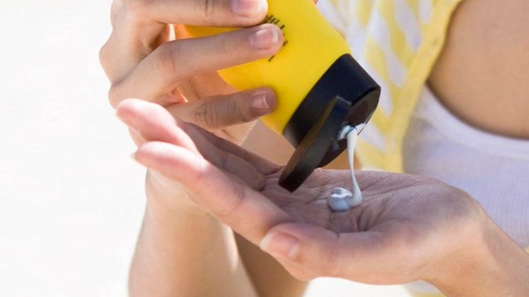 A woman applies sunscreen while at the beach.