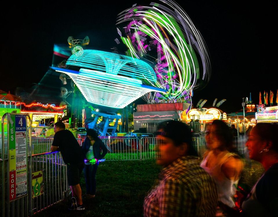 Amusement park rides spin as people attend the