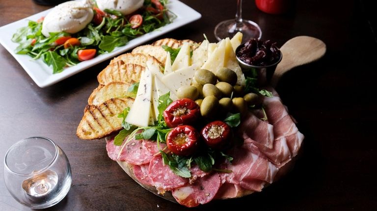 A charcuterie board for two with olives, peppers,