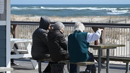 Three women sit at Ponquogue Beach in Hampton
