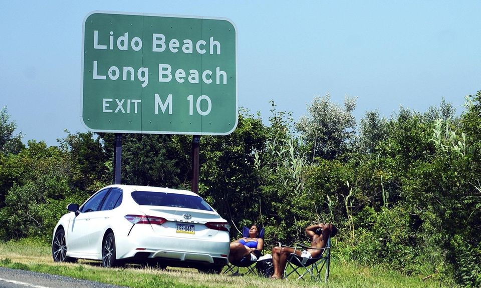 People sunbathe next to their car sitting on