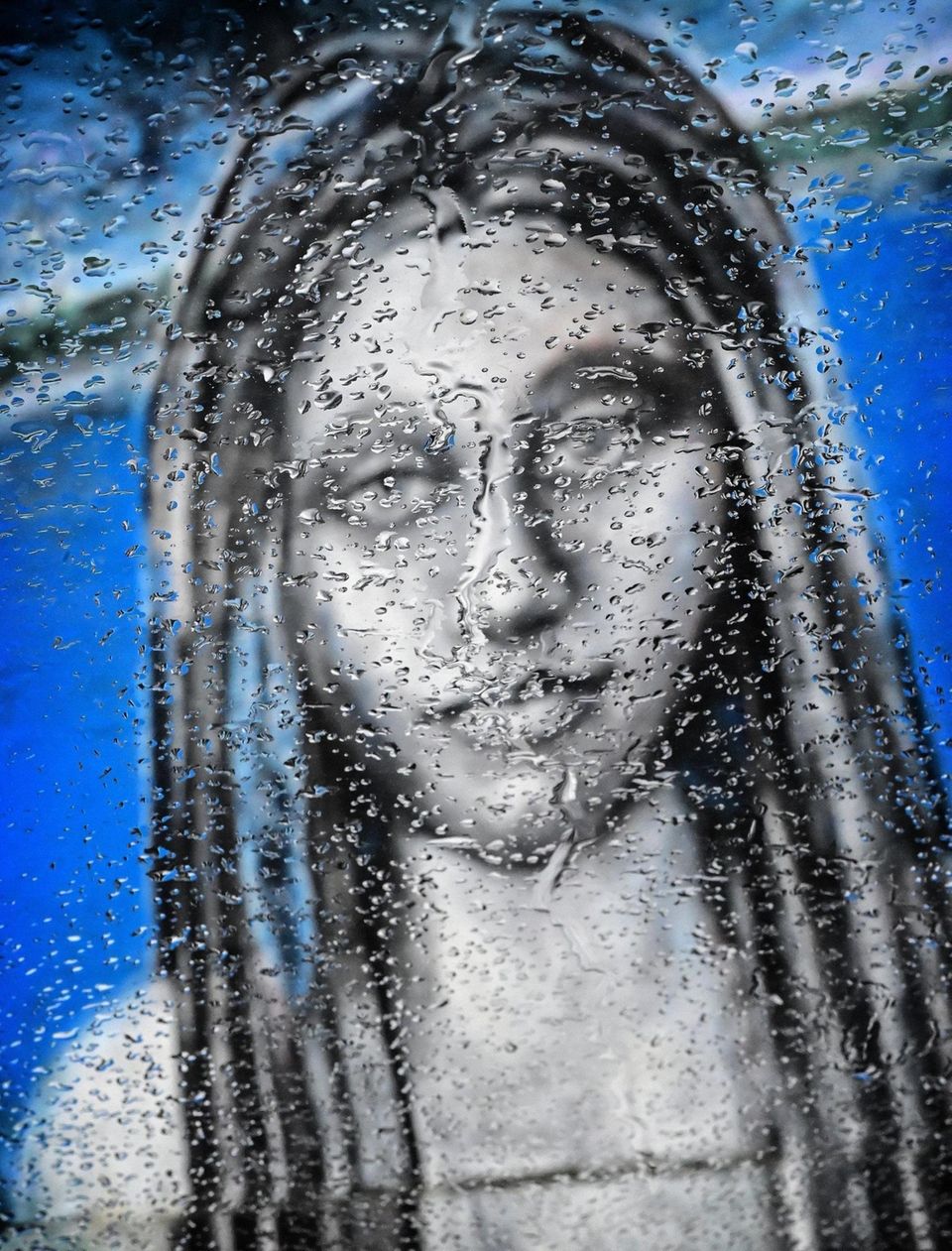 Raindrops collect on a car windshield, obscuring a